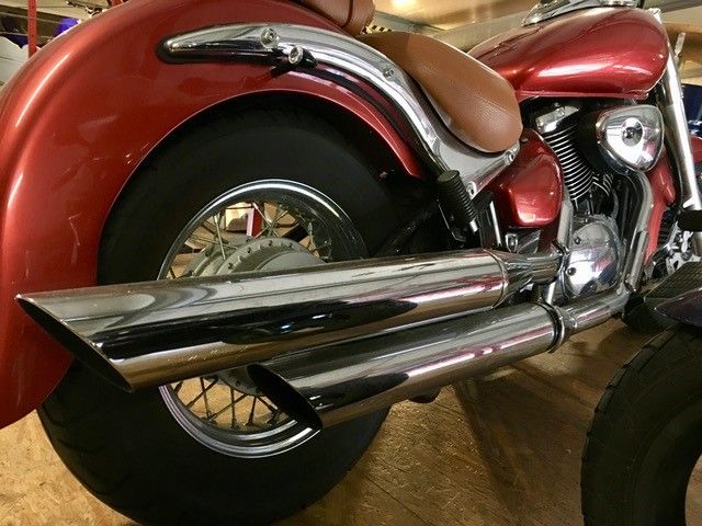 Ein rotes Motorrad mit verchromten Auspuffrohren steht in einer Garage