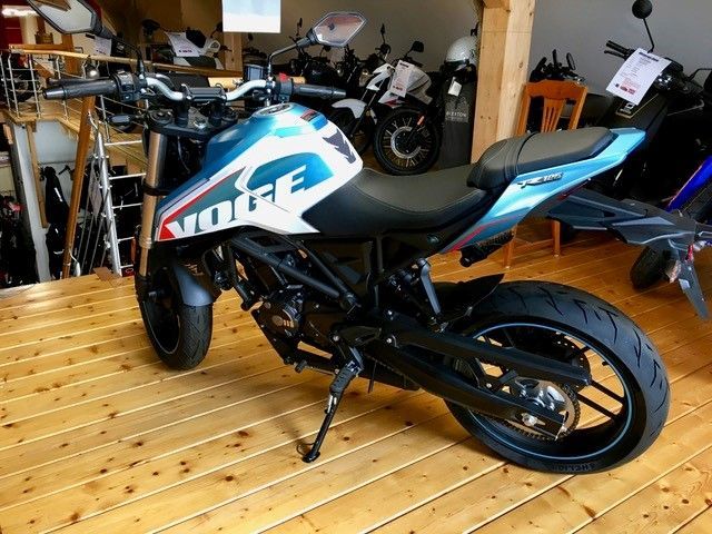 Ein blau-weißes Motorrad steht auf einem Holzboden in einem Ausstellungsraum.