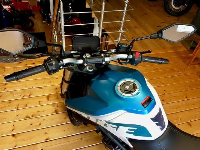 Auf einem Holzboden ist ein blau-weißes Motorrad geparkt.