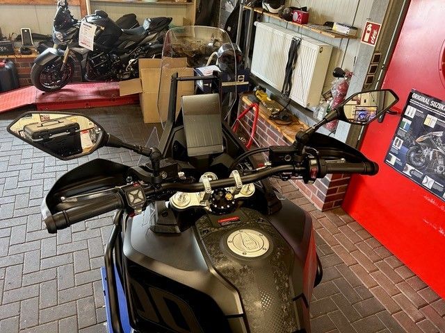 Motorräder parken in einer Garage, im Vordergrund ein schwarzes Motorrad, dahinter ein roter Roller.