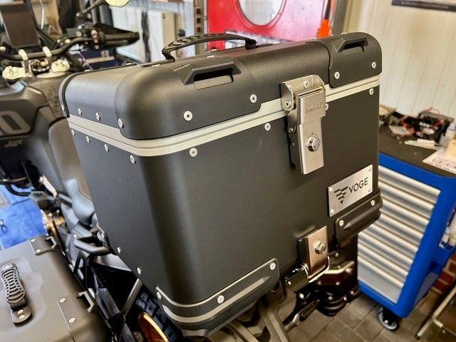 Schwarzer Motorradkoffer mit Metallverschlüssen, montiert an einem Motorrad in einer Garage