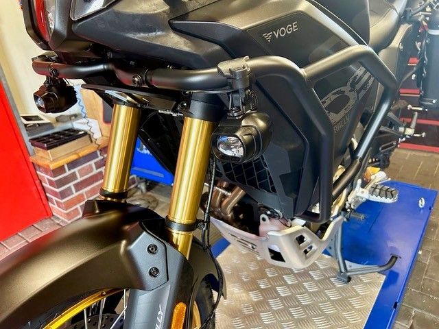 Nahaufnahme der Frontpartie eines Motorrads mit goldener Gabel, schwarzer Verkleidung und silbernen Motorteilen in einer Werkstatt.