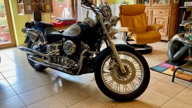 In einem Wohnzimmer ist neben einem Stuhl ein Motorrad geparkt.