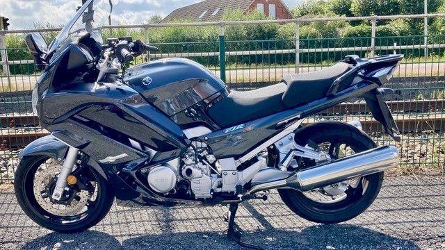 Vor einem Zaun ist ein schwarzes Motorrad geparkt.