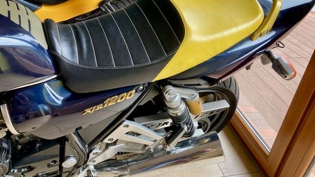 Vor einer Glastür parkt ein blau-gelbes Motorrad.