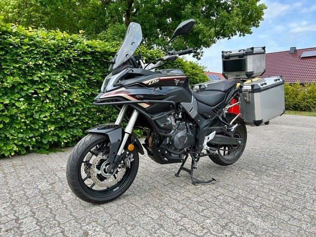 Ein schwarzes Motorrad ist auf einer gepflasterten Auffahrt vor einer Hecke geparkt.
