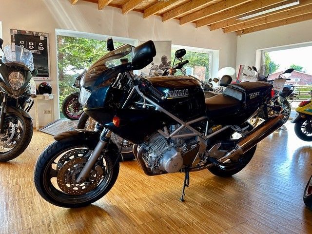 Ein schwarzes Motorrad ist in einem Raum mit anderen Motorrädern geparkt.