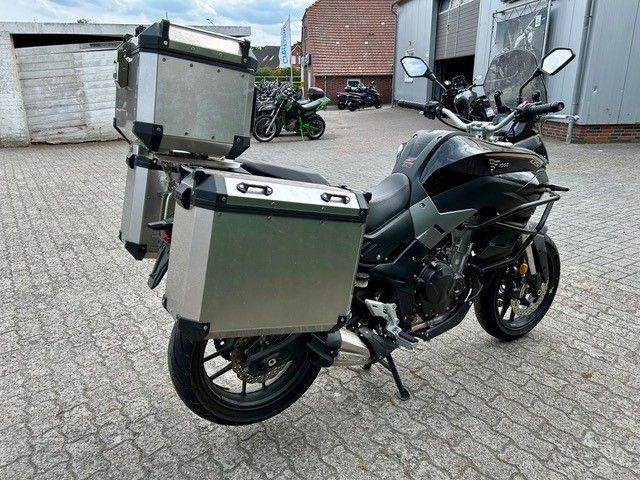 Auf einer gepflasterten Auffahrt vor einer Garage ist ein Motorrad geparkt.