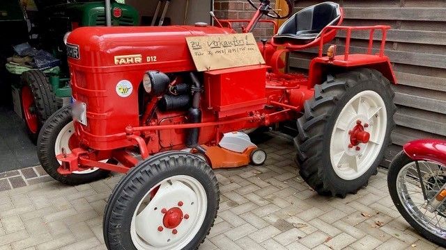 Roter Oldtimer-Traktor mit weißen Rädern, auf Ziegelstein geparkt. Schild auf der Motorhaube.