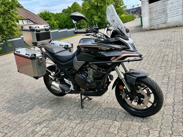 Auf einer gepflasterten Auffahrt ist ein schwarzes Motorrad geparkt.