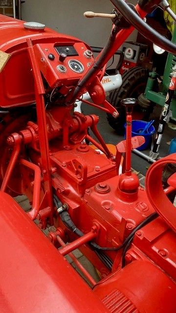 Bedienelemente des roten Traktors: Lenkrad, Anzeigen, Gangschaltung und Hebel. Drinnen, gut beleuchtet.