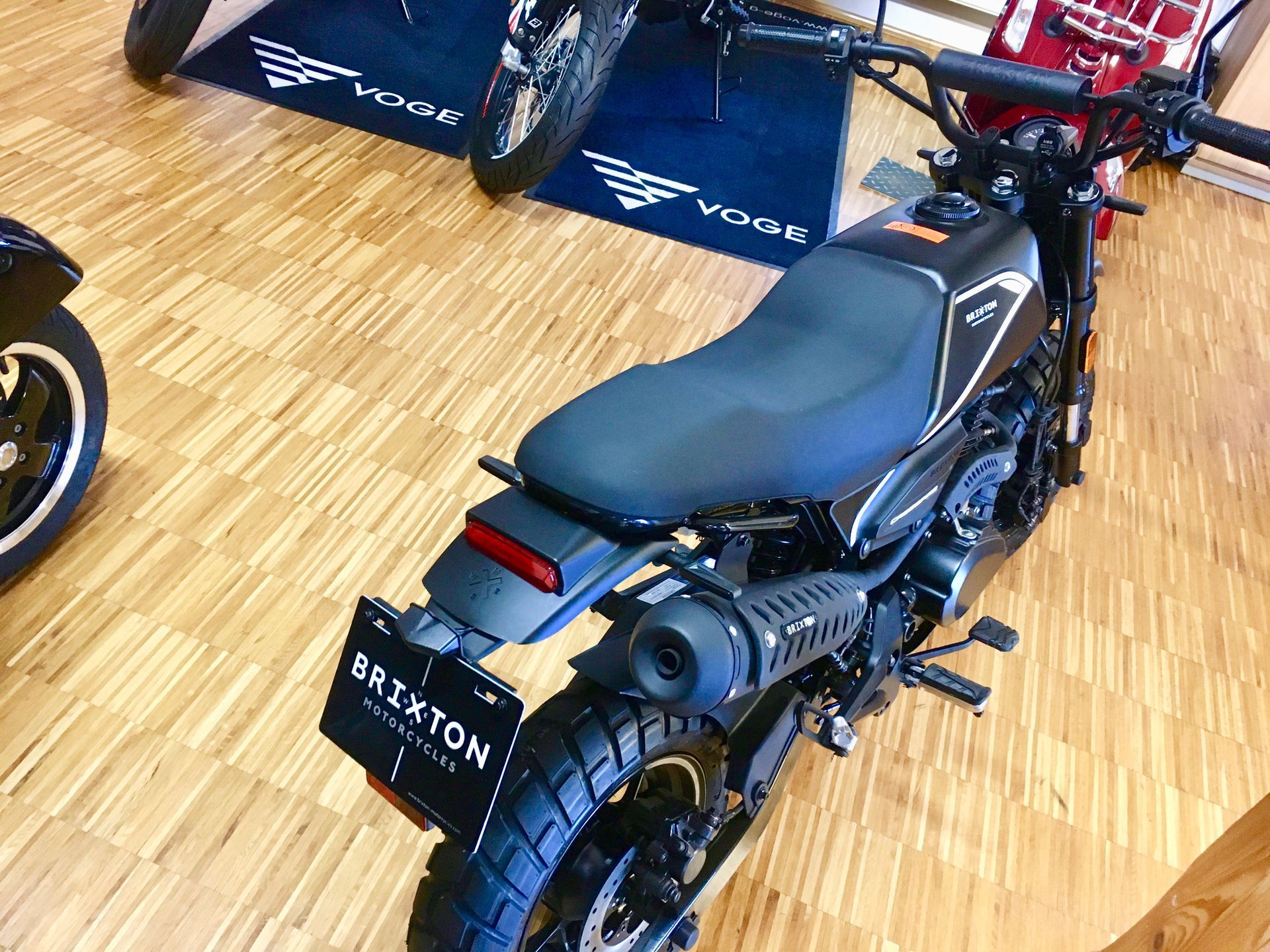 Ein schwarzes Motorrad steht auf einem Holzboden in einem Ausstellungsraum.