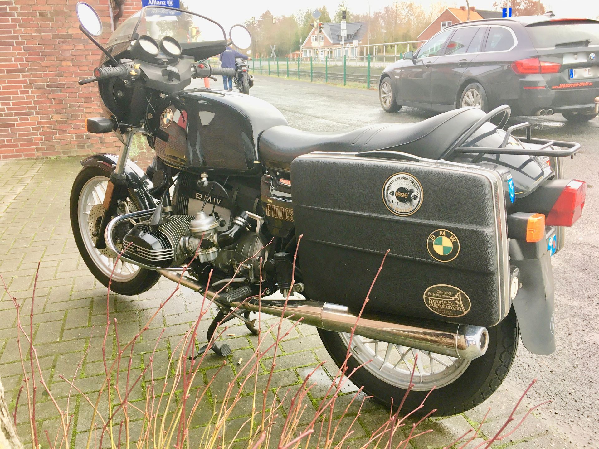 Ein schwarzes Motorrad steht auf einem Parkplatz neben einer Backsteinmauer.