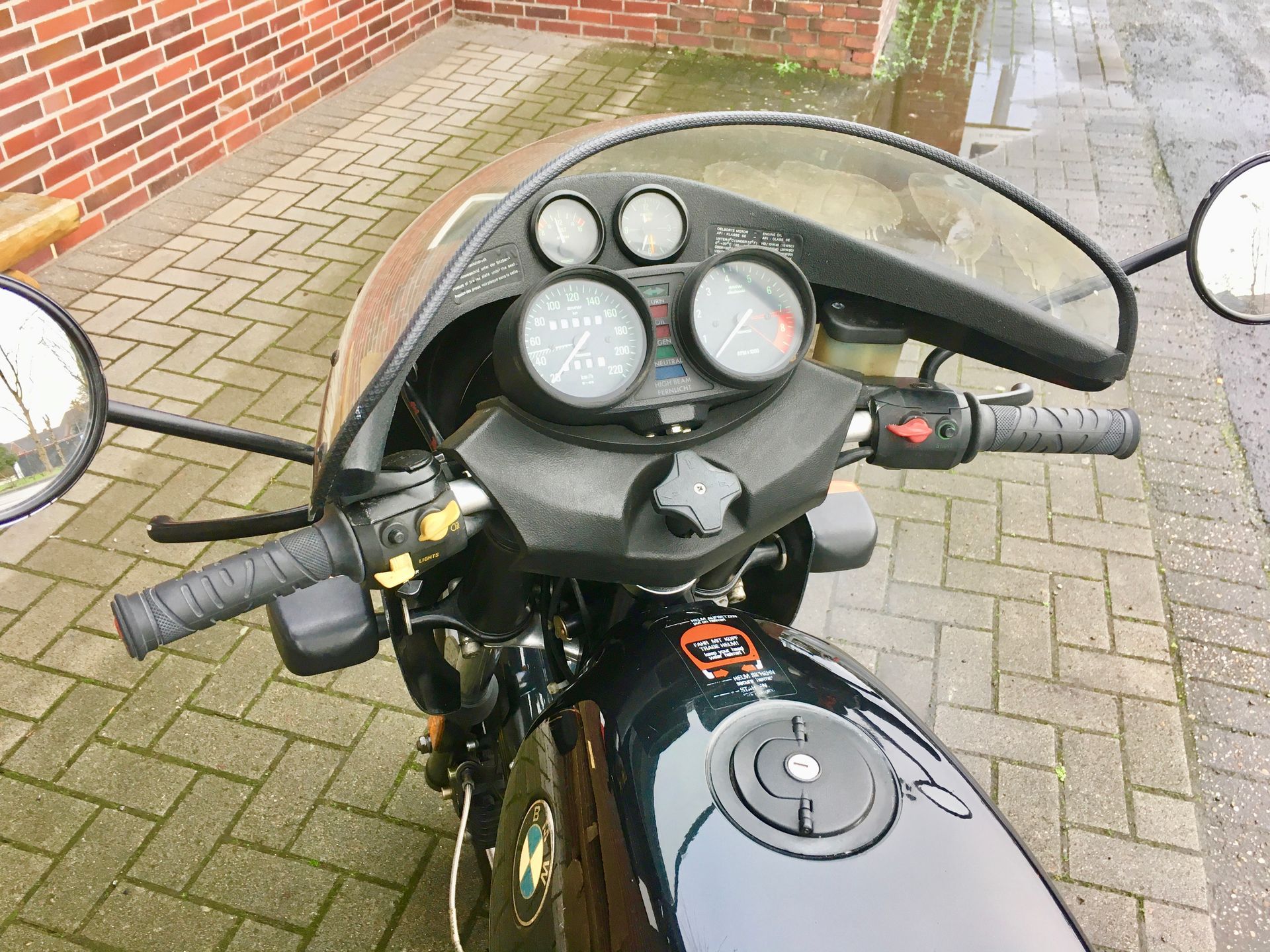 Ein schwarzes Motorrad ist auf einem gepflasterten Gehweg vor einem Backsteingebäude geparkt.