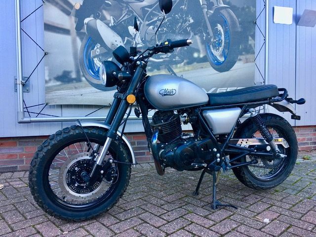 Auf einem gepflasterten Gehweg vor einem Gebäude ist ein Motorrad geparkt.