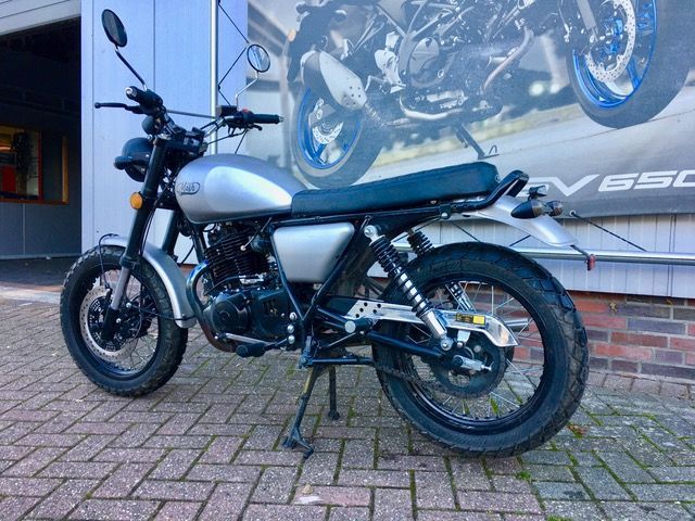 Vor einem Gebäude parkt ein silber-schwarzes Motorrad.