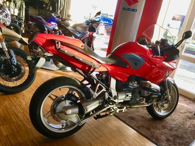 In einem Ausstellungsraum steht neben einem Suzuki-Schild ein rotes Motorrad.