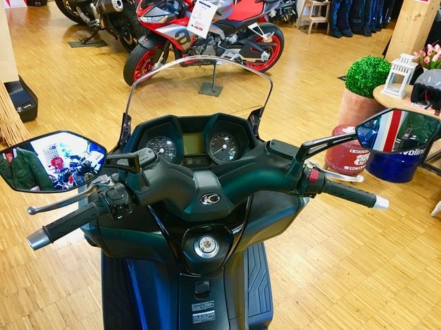 In einem Ausstellungsraum steht ein Motorroller neben einem Motorrad.