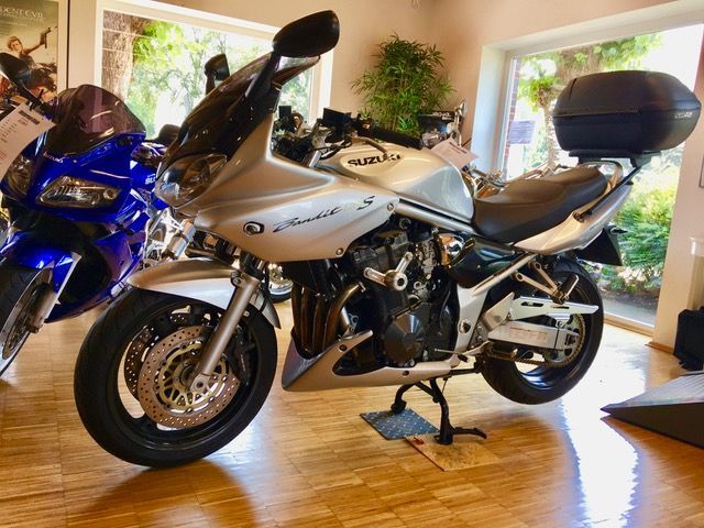 In einem Raum neben einem blauen Motorrad ist ein silbernes Motorrad geparkt.