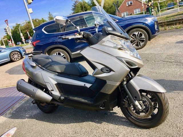 Auf einem Parkplatz steht neben einem blauen SUV ein Motorroller.