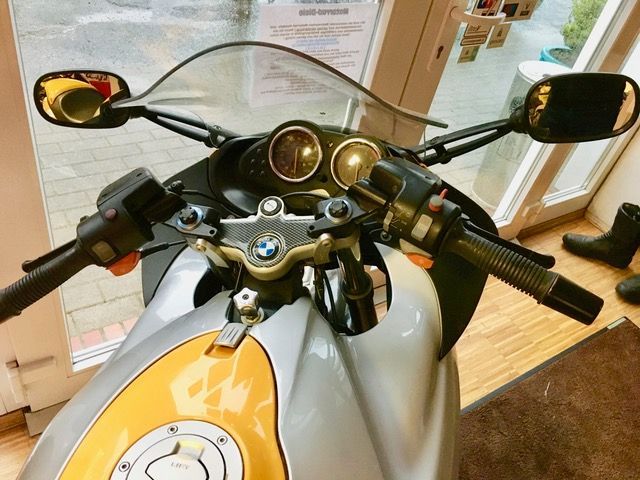 Ein silber-gelbes Motorrad ist vor einem Fenster geparkt