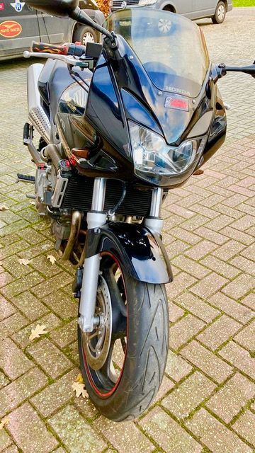 Auf einer gepflasterten Auffahrt ist ein schwarzes Motorrad geparkt.