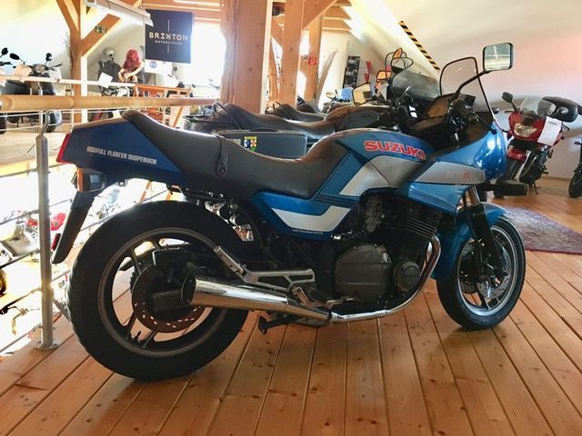 Ein blau-weißes Suzuki-Motorrad ist auf einem Holzboden geparkt