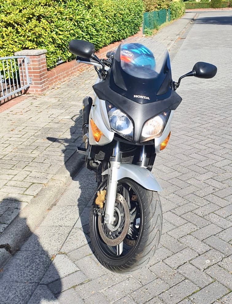 Auf einem gepflasterten Gehweg ist ein Motorrad mit einem Helm auf der Vorderseite geparkt.