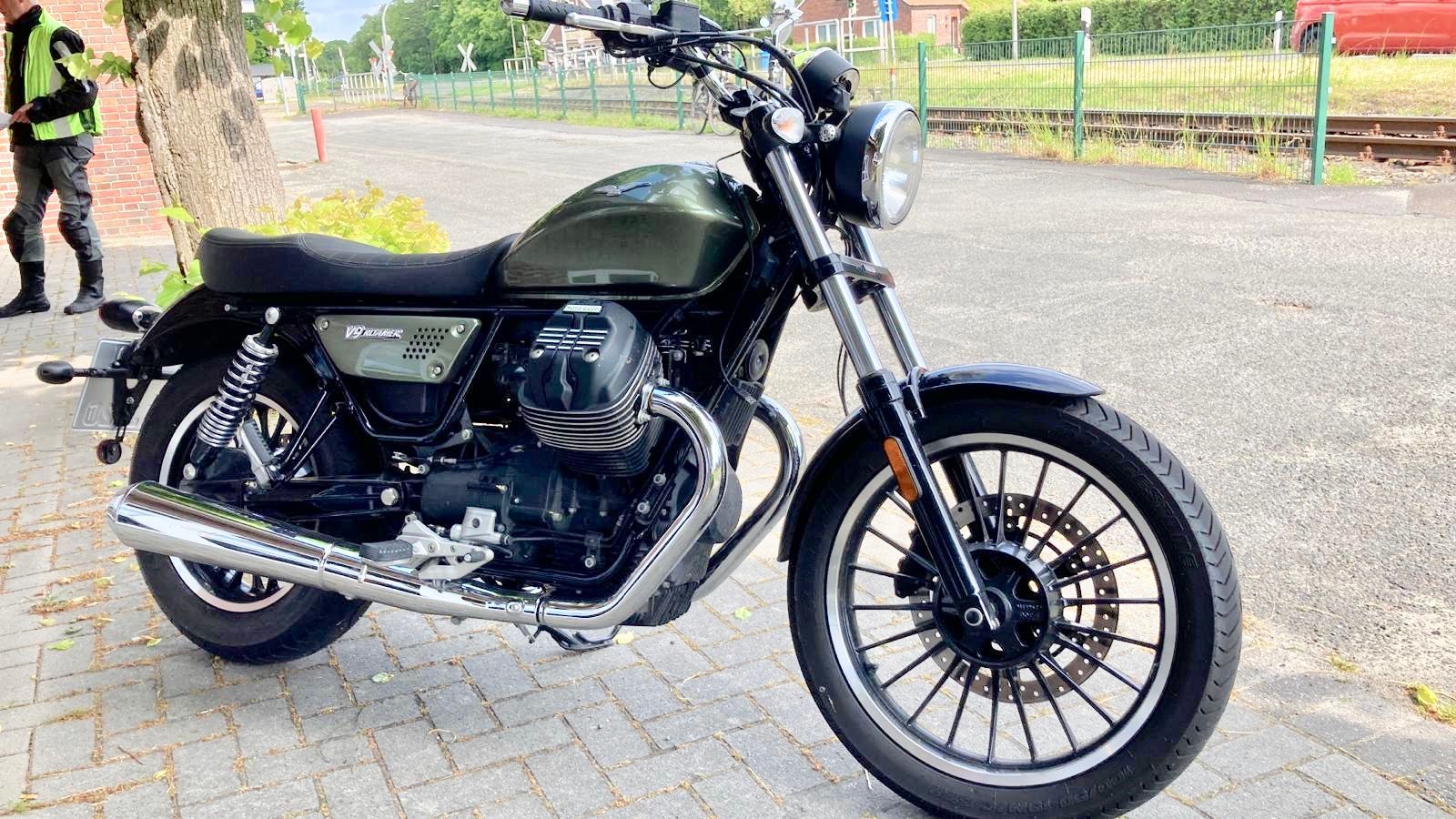 Auf einem Gehweg neben einem Bahngleis ist ein Motorrad geparkt.