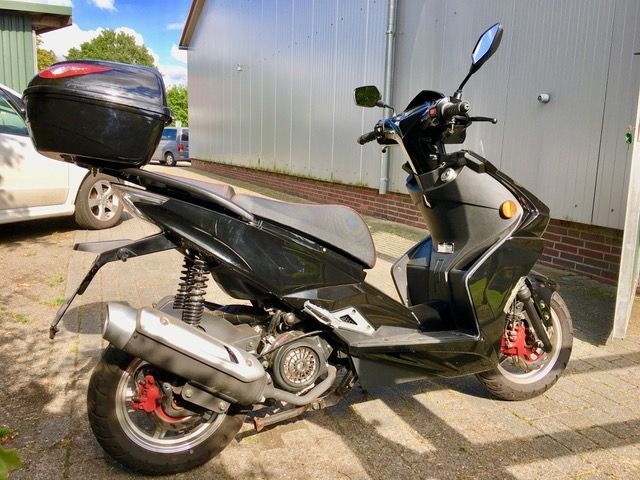 Vor einem Gebäude parkt ein schwarzer Motorroller.