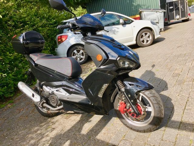 Ein schwarzer Roller steht neben einem weißen Auto