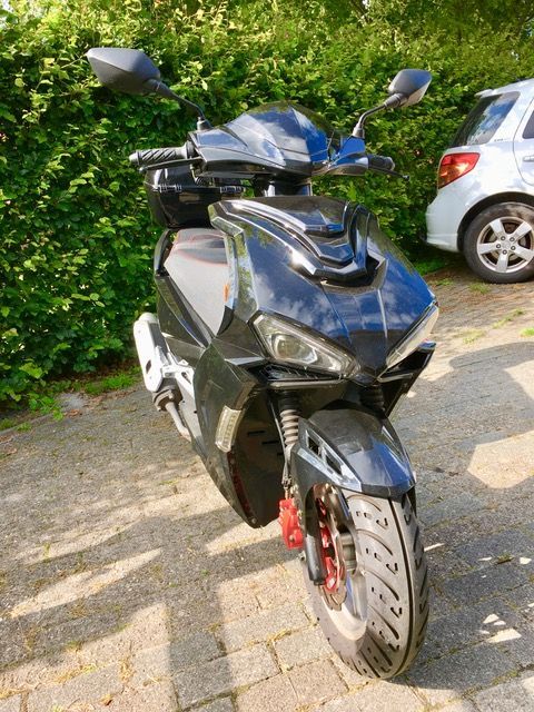 Ein schwarzer Motorroller ist vor einem weißen Auto geparkt.