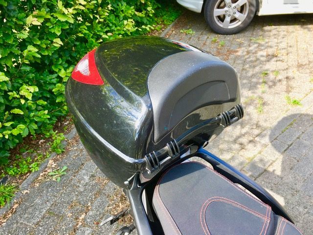 Ein schwarzes Motorrad mit rotem Rücklicht parkt am Straßenrand.