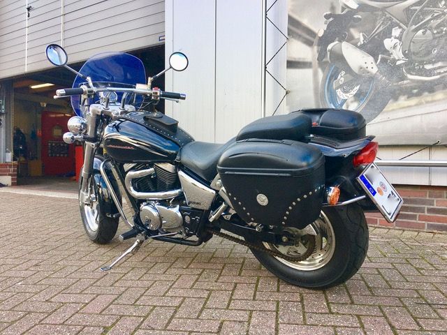 Ein schwarzes Motorrad ist auf einem gepflasterten Gehweg vor einem Gebäude geparkt.