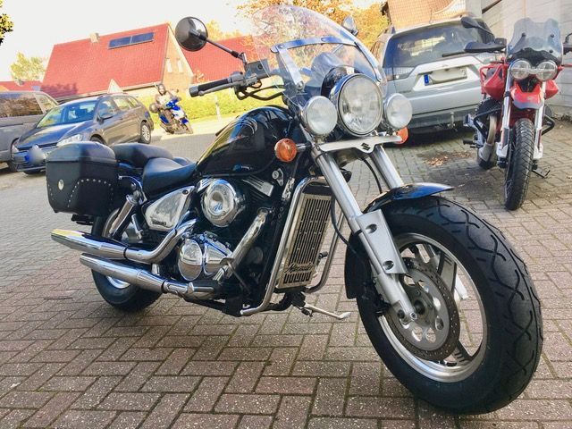 Auf einer gepflasterten Auffahrt ist neben einem Auto ein Motorrad geparkt.