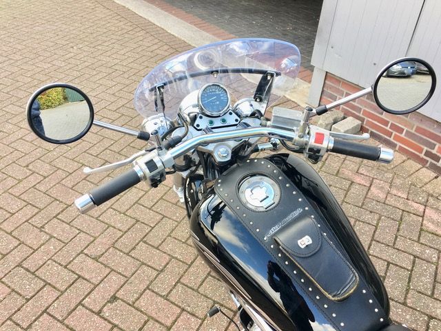 Auf einem gepflasterten Gehweg ist ein schwarzes Motorrad geparkt.