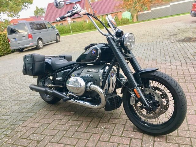 Auf einem gepflasterten Gehweg ist neben einem Lieferwagen ein schwarzes Motorrad geparkt.