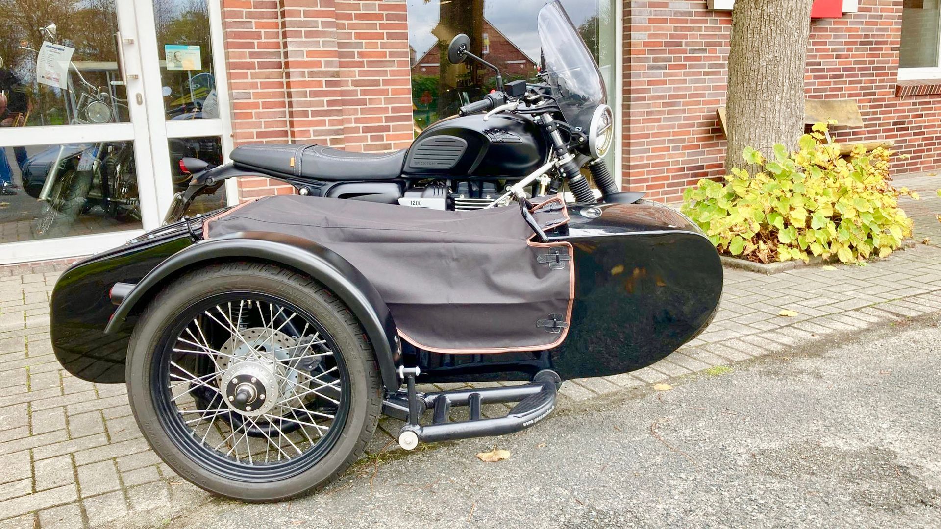 Vor einem Backsteingebäude ist ein Motorrad mit Beiwagen geparkt.