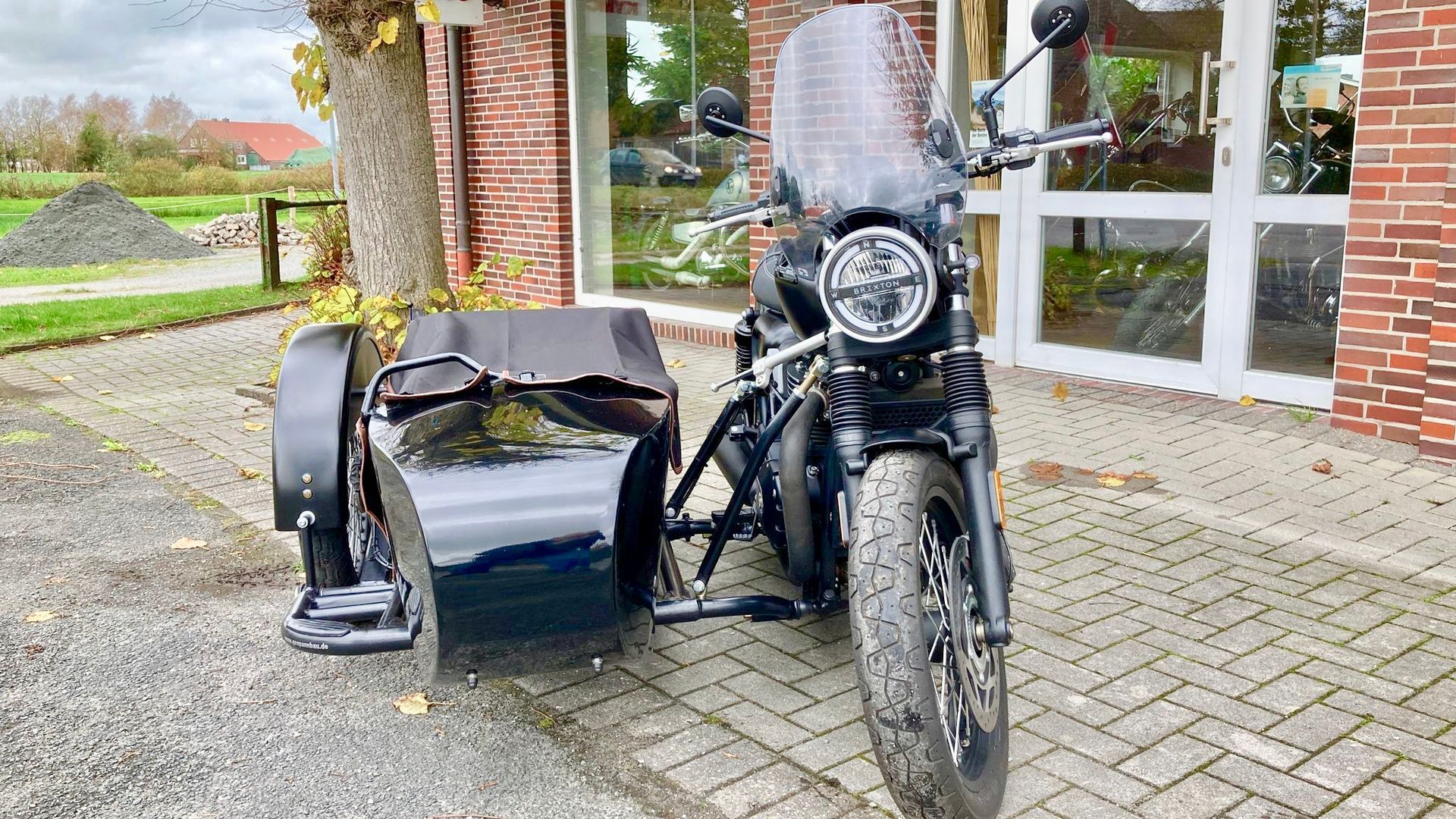 Vor einem Backsteingebäude parkt ein schwarzes Motorrad mit Beiwagen.