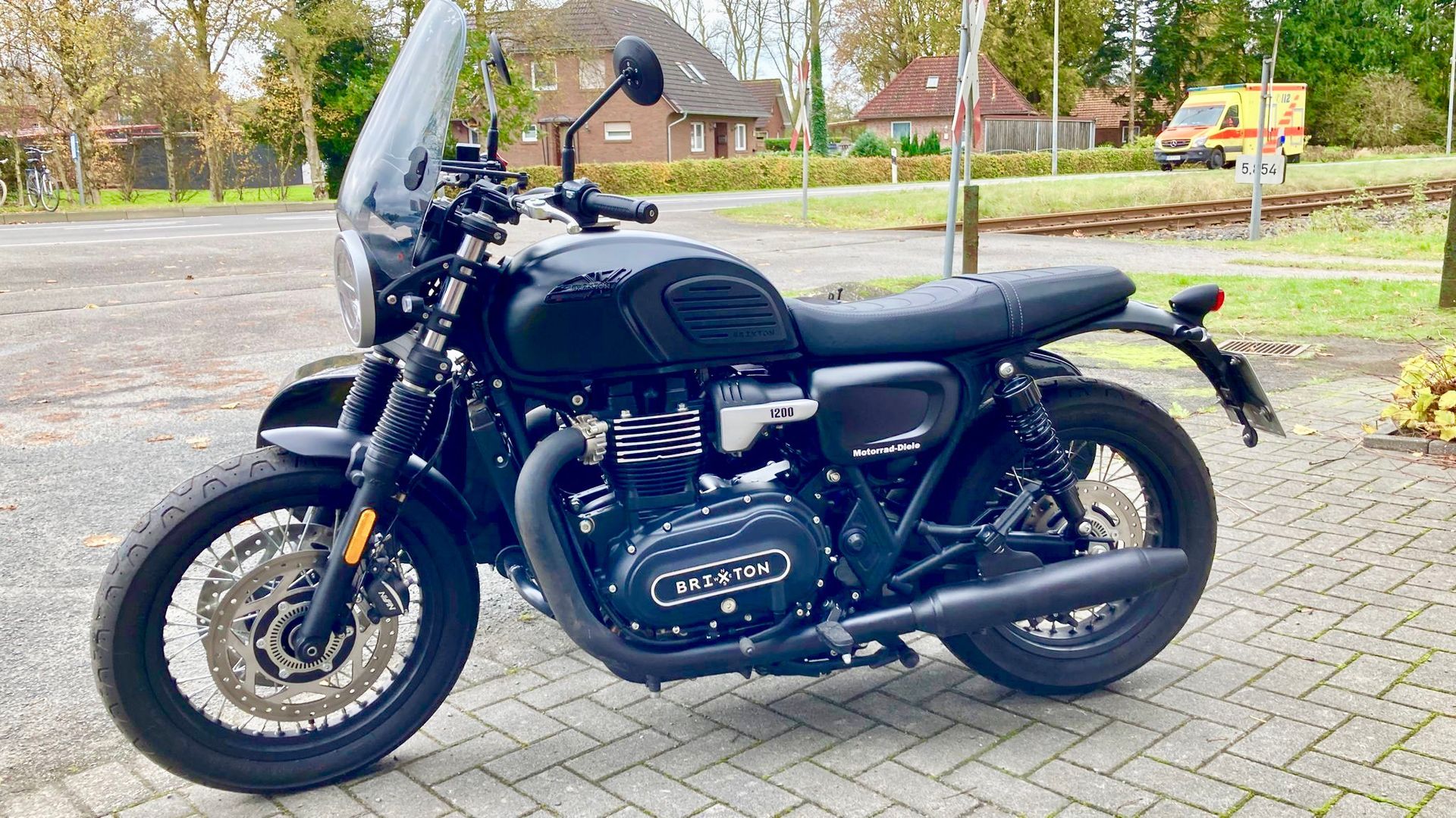 Auf einem gepflasterten Gehweg ist ein schwarzes Motorrad mit Windschutzscheibe geparkt.