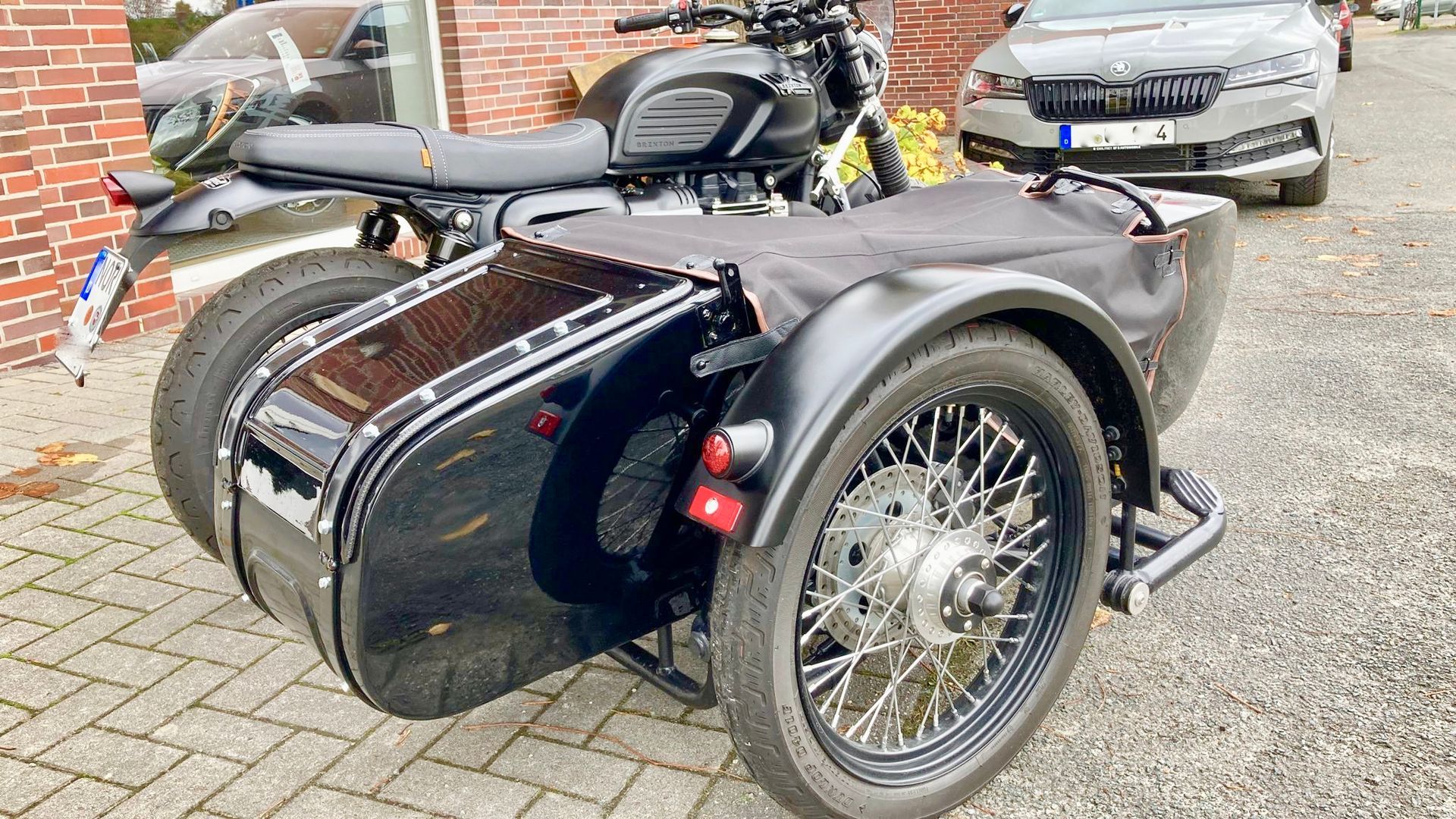 Vor einem Backsteingebäude parkt ein schwarzes Motorrad mit Beiwagen.