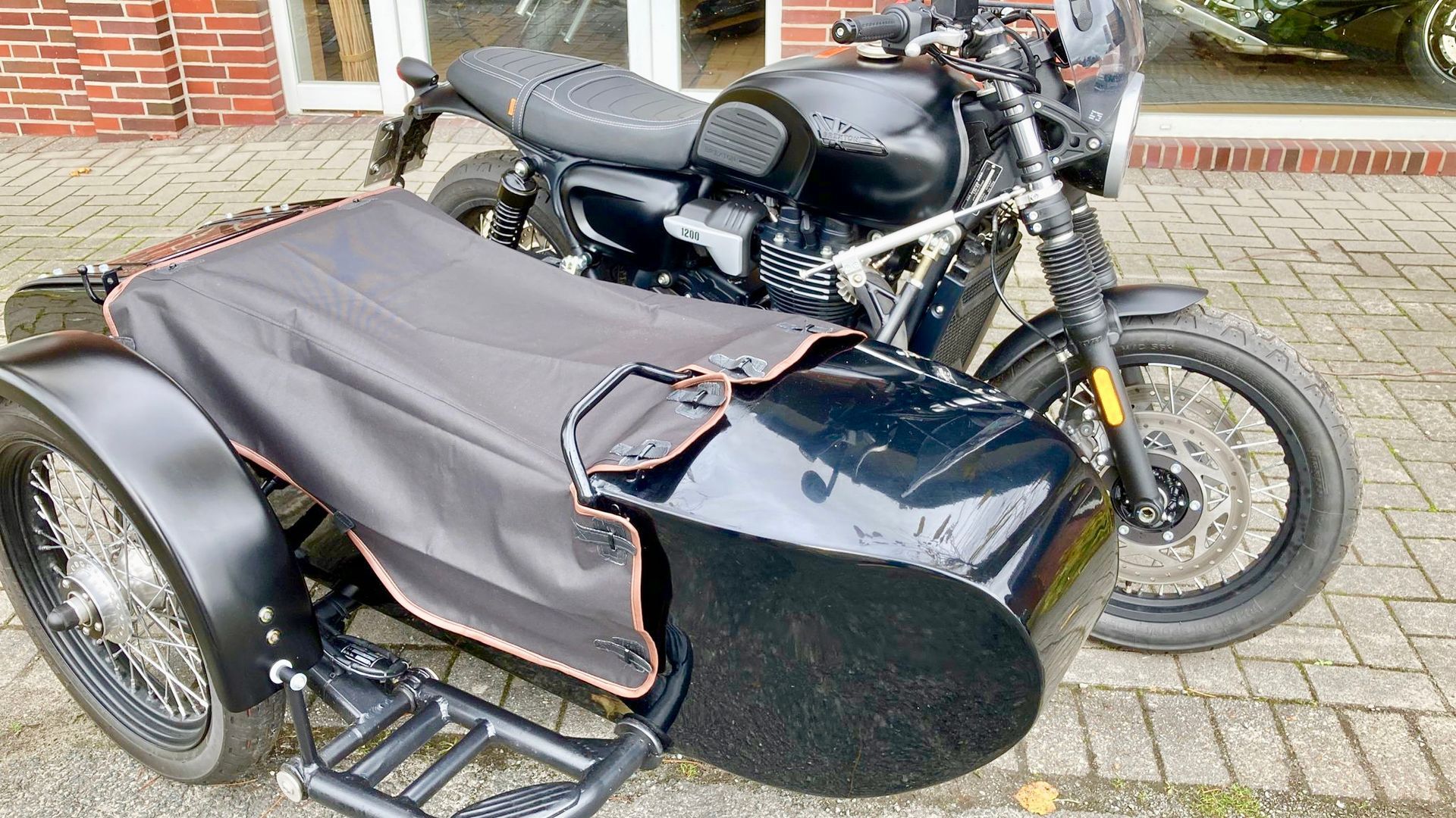 Vor einem Backsteingebäude parkt ein schwarzes Motorrad mit Beiwagen.