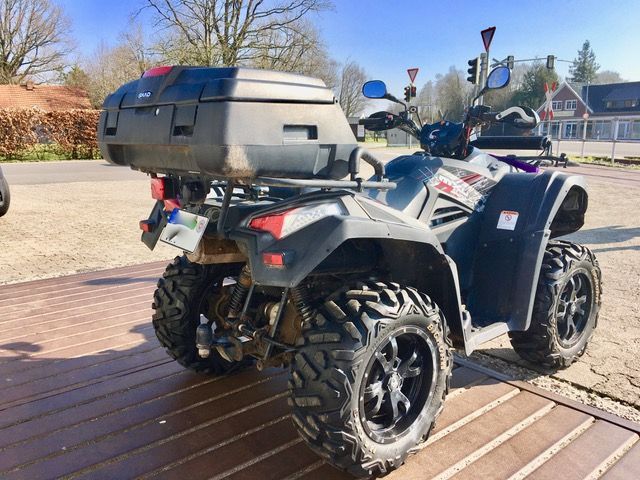 Auf einem Holzdeck ist ein Quad mit einer großen Kiste auf der Ladefläche geparkt.