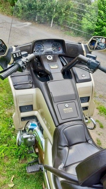 Draufsicht auf ein gold-schwarzes Honda Goldwing-Motorrad. Armaturenbrett, Lenker und Sitz sind sichtbar, im Freien geparkt.