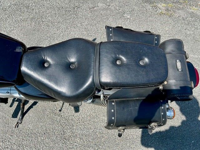 Ein schwarzes Motorrad mit Ledersitz und Satteltaschen ist am Straßenrand geparkt.