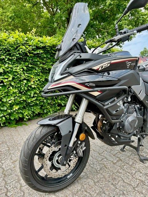 Vor einer Hecke parkt ein schwarzes Motorrad.