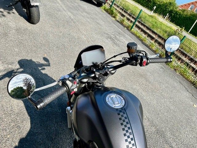 Ein dunkelgraues Motorrad mit einem karierten Muster auf dem Kraftstofftank, aus der Perspektive des Fahrers betrachtet.