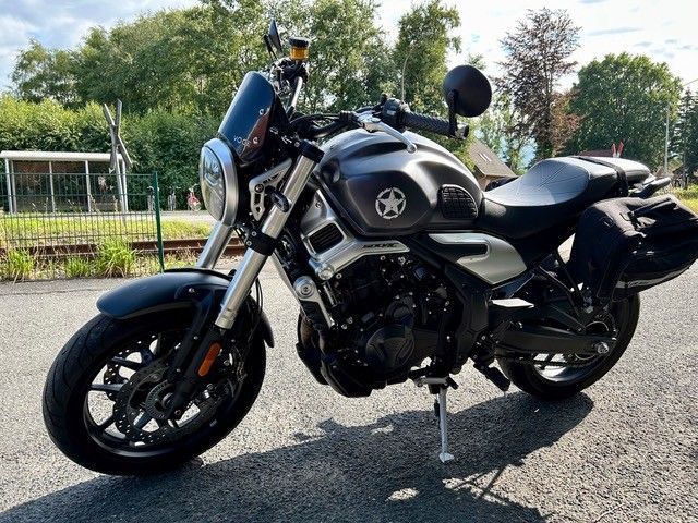 Auf dem Bürgersteig geparktes schwarzes Motorrad mit Beifahrersitz, Gepäck und kleiner Windschutzscheibe.