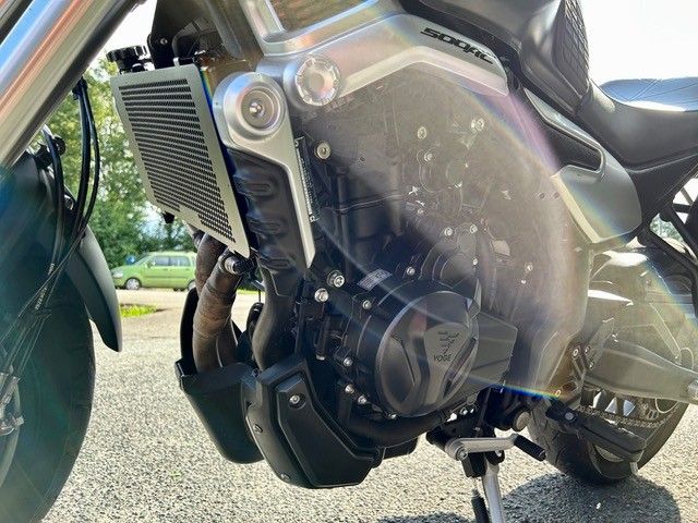 Seitenansicht eines silber-schwarzen Motorradmotors, Kühlers und Frontverkleidung. Es ist im Freien auf Asphalt geparkt.