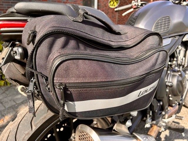 Schwarze Motorrad-Satteltasche, befestigt an einem grauen Motorrad, mit einem reflektierenden Streifen.
